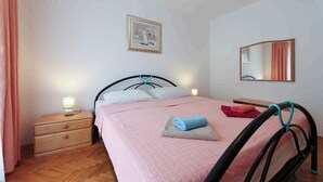 A bedroom with a bed, a nightstand, a bedside lamp, a framed picture on the wall, and a mirror. - Holiday apartment with air conditioning and garden (Jadranovo)