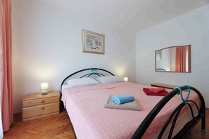 Ein Schlafzimmer mit einem Bett, einem Nachttisch, einer Nachttischlampe, einem gerahmten Bild an der Wand und einem Spiegel.
