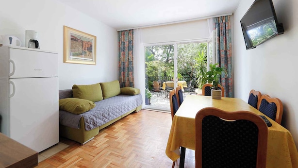 A compact living space with a kitchenette, a sofa, a dining table with chairs, a TV mounted on the wall, and a sliding glass door leading to an outdoor area. - Holiday apartment with air conditioning and garden (Jadranovo)