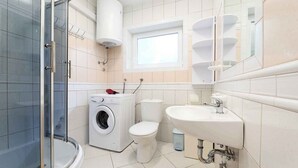A bathroom with a glass shower enclosure, a washing machine, a toilet, and a sink. - Holiday apartment with air conditioning and garden (Jadranovo)