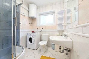 Ein Badezimmer mit Duschkabine aus Glas, Waschmaschine, Toilette und Waschbecken.