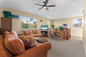 Ein Wohnzimmer mit Sofa, Fernseher, Essbereich und Deckenventilator.