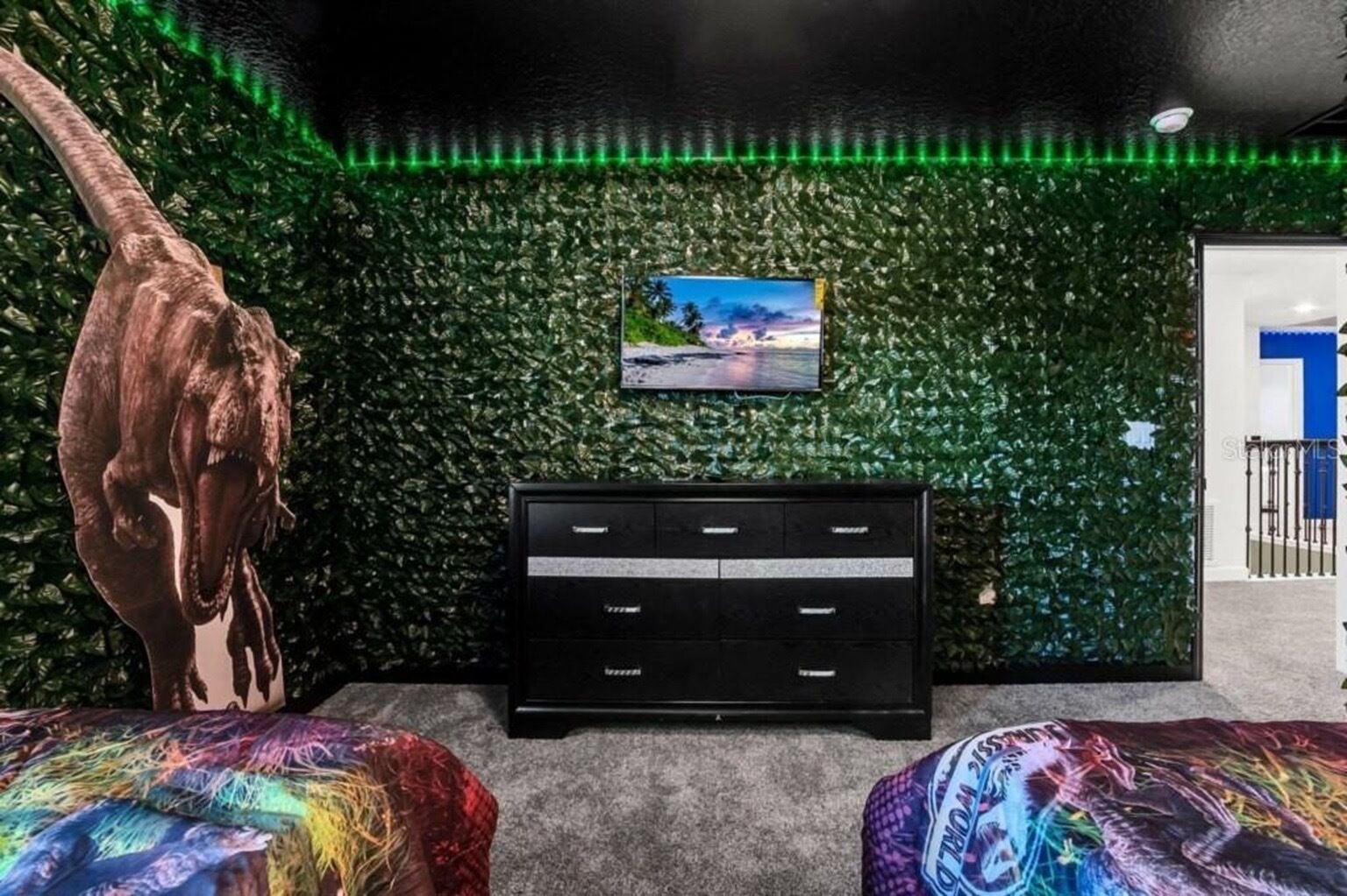 Une pièce avec un mur recouvert de verdure, un meuble de rangement noir et un téléviseur fixé au mur.