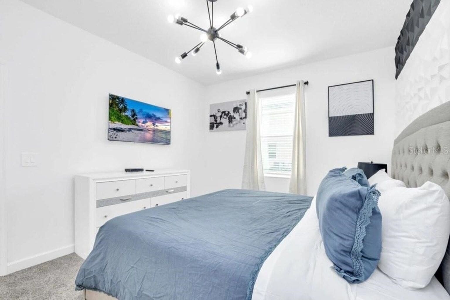 A bedroom with a bed, a dresser, a ceiling light fixture, and a window with curtains.
