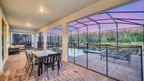 A covered outdoor patio with a pool, seating area, and a view of the surrounding landscape. - Beautiful 9-bedroom house with AC in serene Kissimmee , Bring the whole Family ! (Kissimmee)