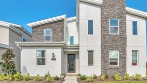 A modern multi-story residential building with a stone facade, a central entrance, and a well-maintained front yard. - Beautiful 9-bedroom house with AC in serene Kissimmee , Bring the whole Family ! (Kissimmee)