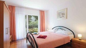 Quarto com cama, mesa de cabeceira, guarda-roupa e janela com cortinas.