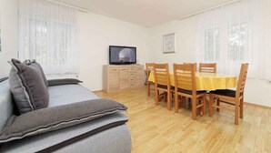 Um quarto com sofá, televisão, mesa de jantar com cadeiras e um armário de madeira.