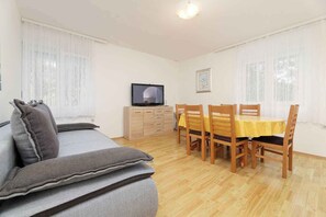 A room with a sofa, a TV, a dining table with chairs, and a wooden cabinet. - Holiday apartment with air conditioning and garden (Jadranovo)
