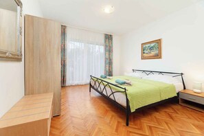 A bedroom with a bed, a nightstand, a mirror, and a window with curtains. - Holiday apartment with air conditioning and garden (Jadranovo)