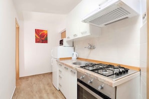 A compact kitchen with white cabinets, a gas stove, a microwave, and a kettle. - Holiday flat pleasantly overlooking the courtyard and garden (Jadranovo)