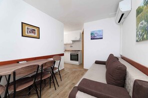 A compact living space with a kitchenette, a dining area with a table and chairs, and a sofa. - Holiday flat pleasantly overlooking the courtyard and garden (Jadranovo)