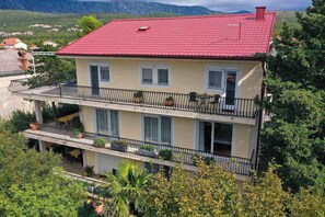 A two-story building with balconies, a red roof, and surrounding greenery. - Holiday flat pleasantly overlooking the courtyard and garden (Jadranovo)