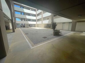 Um amplo pátio interno com piso de azulejos, um canteiro central e um edifício em vários níveis ao fundo.