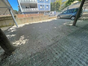 Ein gepflasterter Bereich mit Kiesbelag, einem Metallzaun und einem in der Nähe geparkten, blauen Auto.