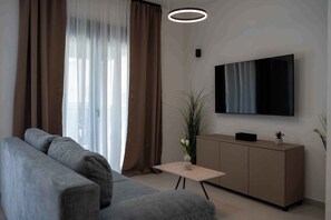 A modern living room with a grey sofa, a small table with a vase, a cabinet, and a mounted TV. - Holiday home with hot tub and terrace (Sukošan)