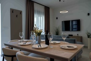 A modern dining area with a long table, chairs, wine glasses, and a vase with flowers. - Holiday home with hot tub and terrace (Sukošan)