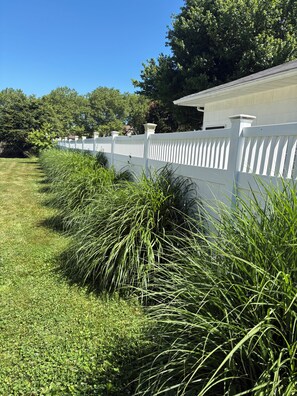A white fence with a row of tall grass in front. - Cute 3-bedroom ranch in heart of Southampton village (Southampton)
