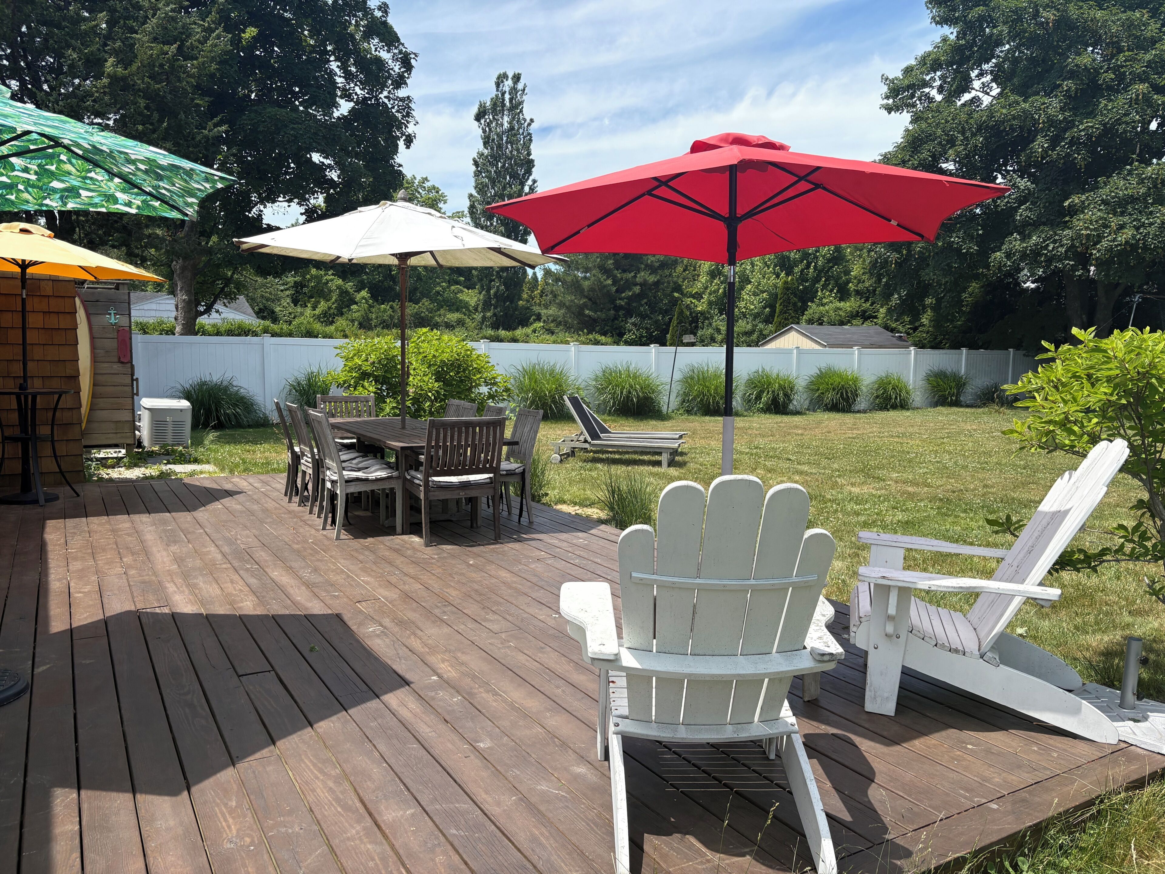 A wooden deck with a table and chairs, a red umbrella, and a white chair.