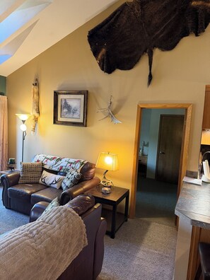 Ein Wohnzimmer mit einer Couch, einem Couchtisch, einer Lampe, einem gerahmten Bild und einem aufgehängten Tierfell.