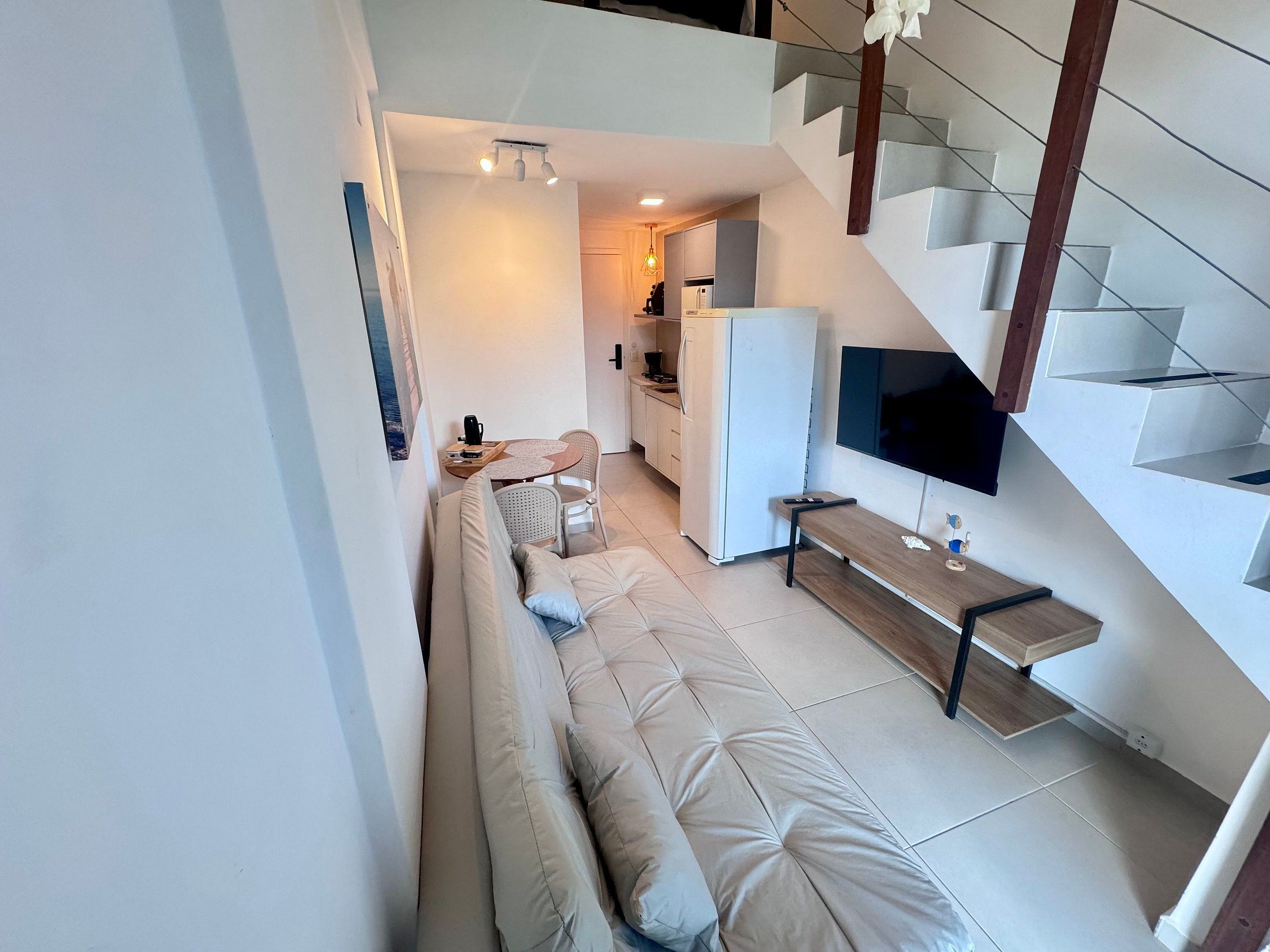 Un espacio habitable moderno con sofá, zona de comedor, cocina y televisor montado en la pared.