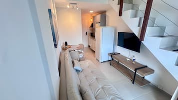 Un espacio habitable moderno con sofá, zona de comedor, cocina y televisor montado en la pared.