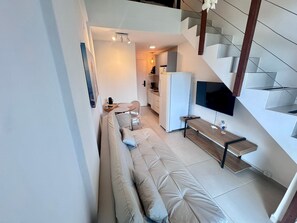 Un espacio habitable moderno con sofá, zona de comedor, cocina y televisor montado en la pared.