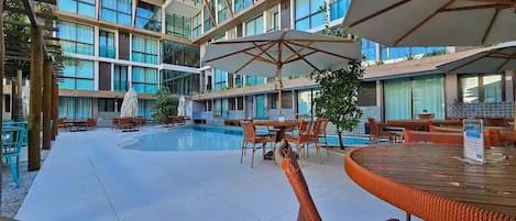 A hotel pool area with multiple levels of balconies, outdoor seating, and umbrellas.