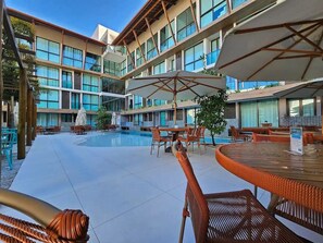 Zona de piscina de hotel con varios niveles de balcones, mobiliario exterior y sombrillas.
