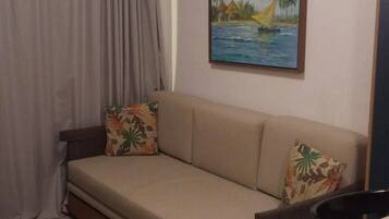 Una habitación con un sofá, un cuadro de una escena tropical, una cortina y una silla amarilla.