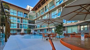 A hotel courtyard with a swimming pool, outdoor seating, and a multi-story building with large windows. - Sunny Hall By Flat na Praia (Ipojuca)