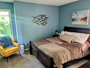 Ein Schlafzimmer mit einem Bett, einem Sessel, einem Wandbild und einem Fenster.