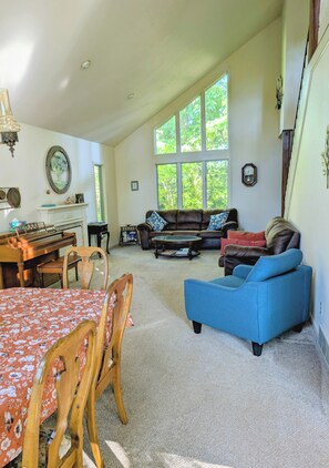 Ein geräumiges Wohnzimmer mit einem Klavier, einem blauen Sofa und einem Essbereich mit einem blumigen Tischläufer.