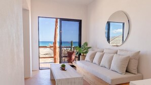 A modern living room with a sofa, a coffee table, and a large window overlooking a beach.