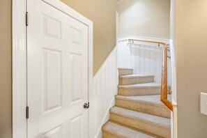 A white door with a modern handle, a carpeted staircase with a wooden handrail, and a light-colored wall. - Northshore Lookout: Golf & Beach Retreat (Nags Head)
