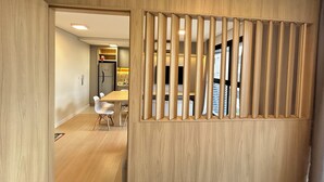 Een modern interieur met een houten scheiding, een eethoek met witte stoelen, en een keuken met een koelkast en kasten.
