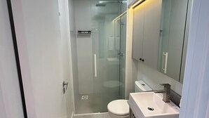 Een moderne badkamer met een douchecabine van glas, een wit toilet en een wastafel met spiegel.