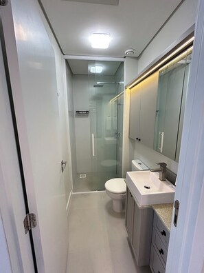 Un baño moderno con cabina de ducha de vidrio, inodoro blanco y tocador con espejo.