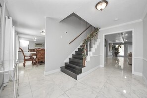 A staircase with a wooden handrail and a plant decoration, leading to a room with a dining table and chairs. - Spacious Pool Home Near IAH Accommodates Families and Groups (houston)