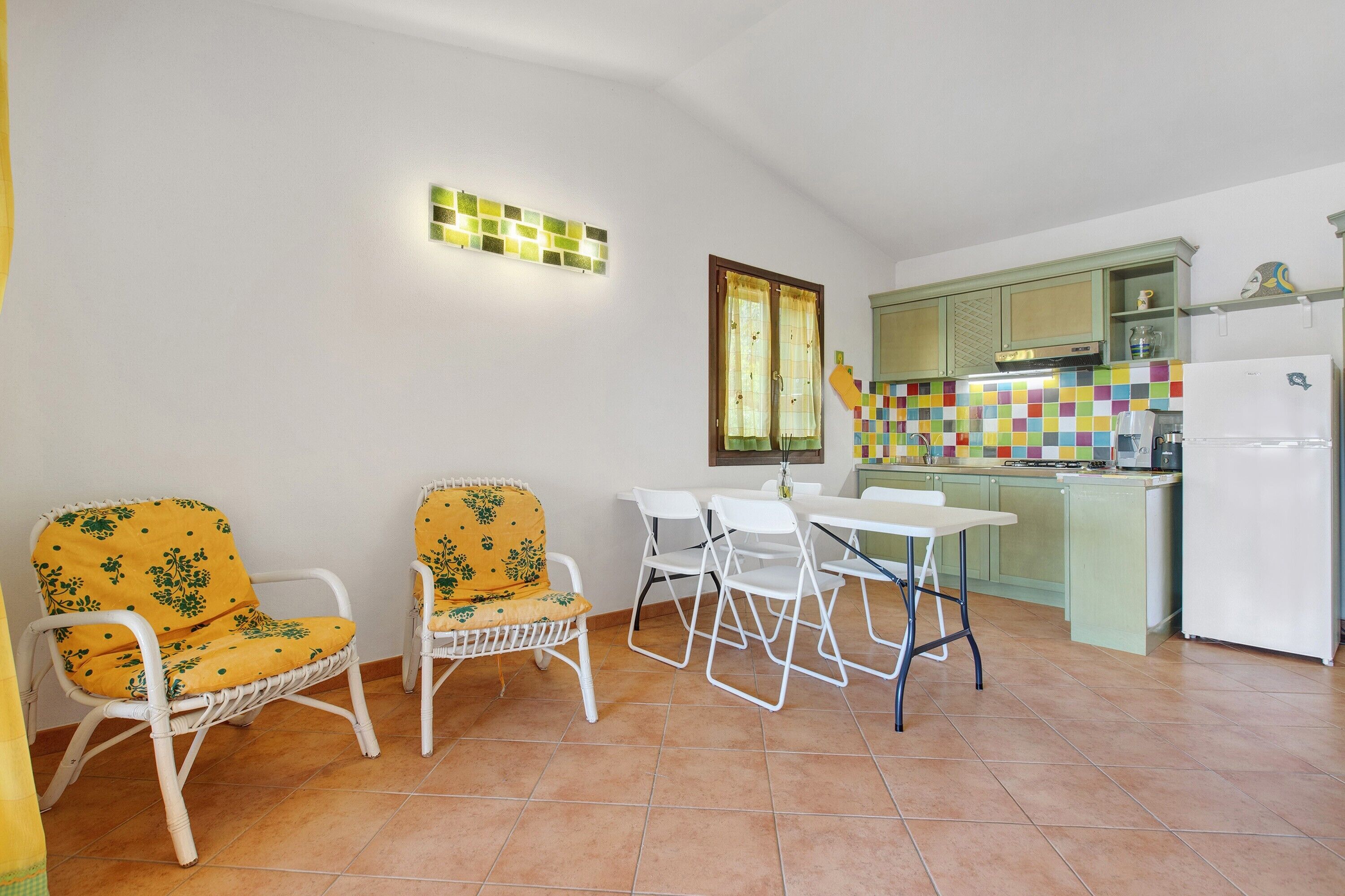 Cozinha compacta com área de refeições, apresentando um painel de azulejos, geladeira e janela com cortinas.