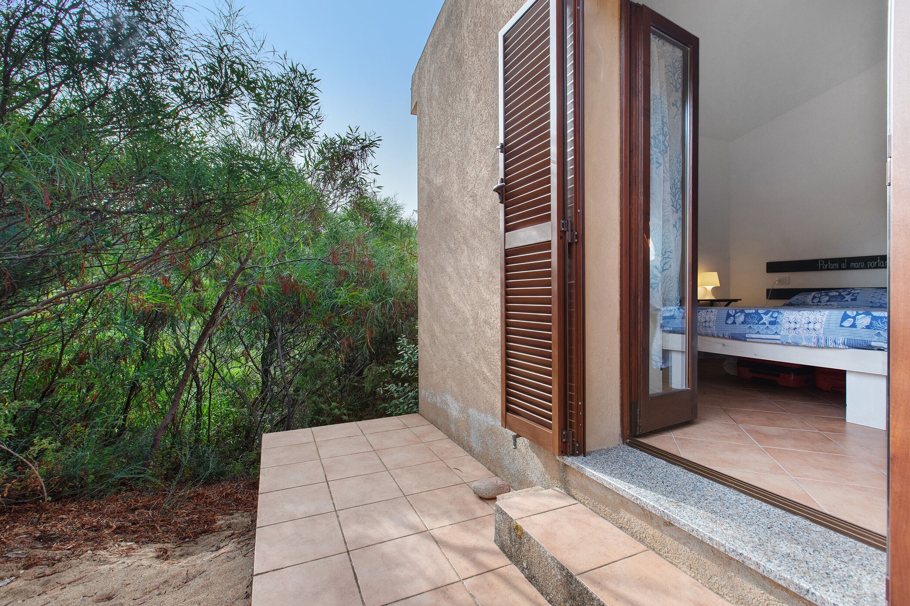 Quarto com cama, mesa de cabeceira e janela com vista para árvores.