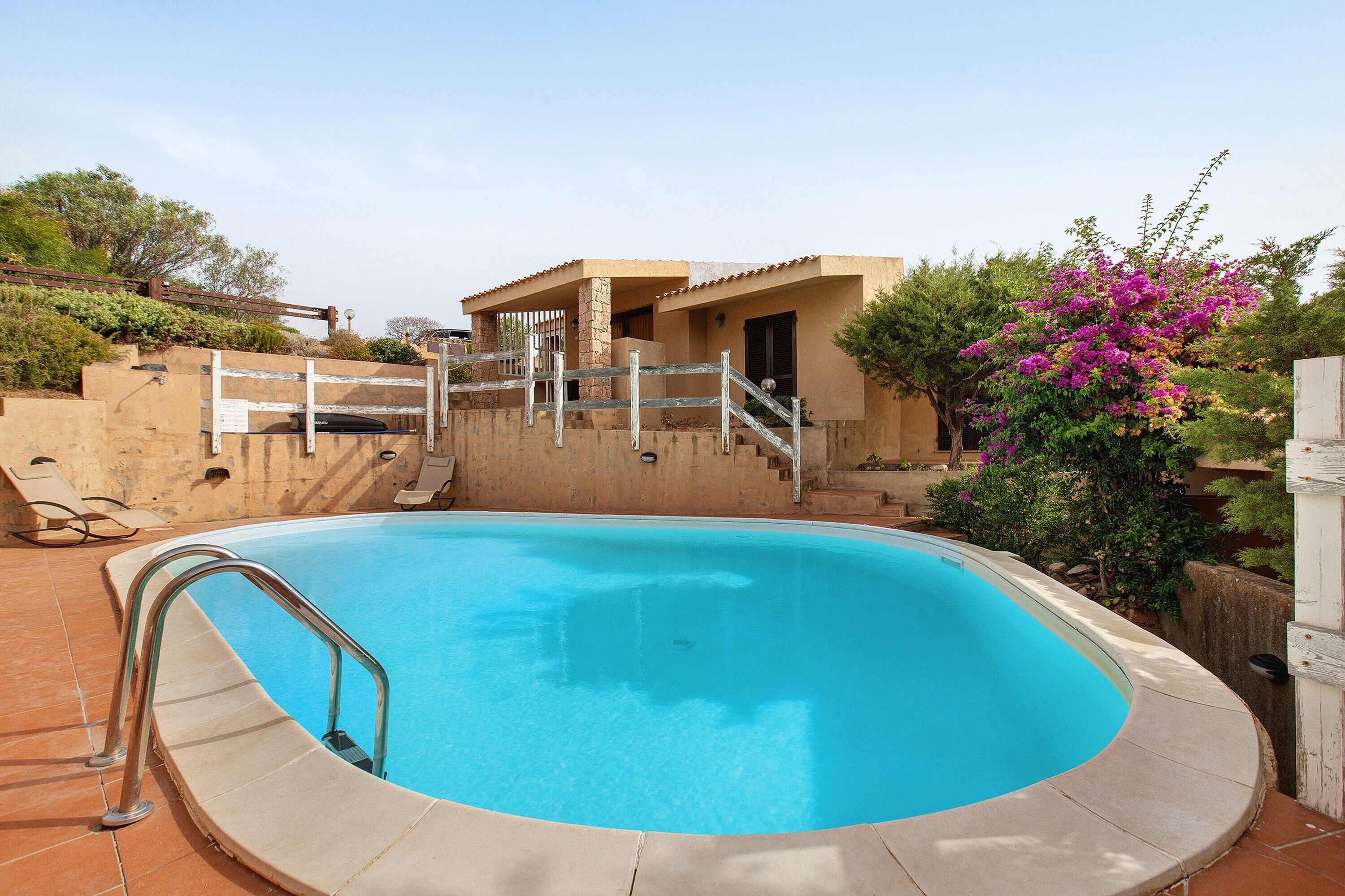 Piscina com escada de metal, área de estar coberta e edifício com fachada de pedra.