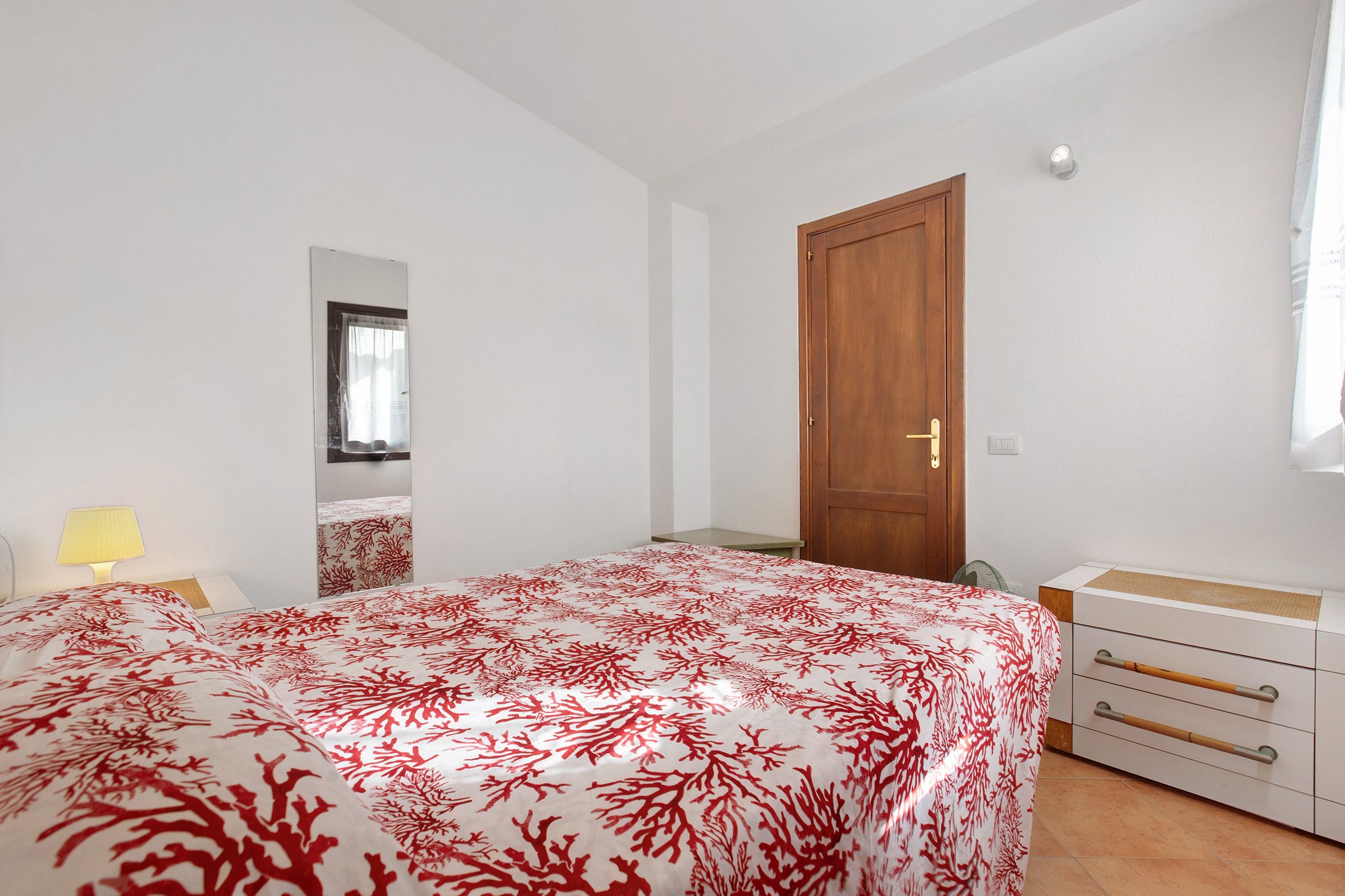 Un dormitorio con cama, mesita de noche, lámpara, armario y puerta.