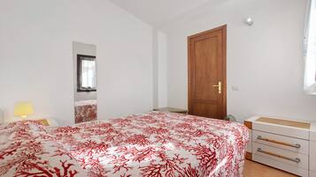 Quarto com cama, mesa de cabeceira, abajur, guarda-roupa e uma porta.
