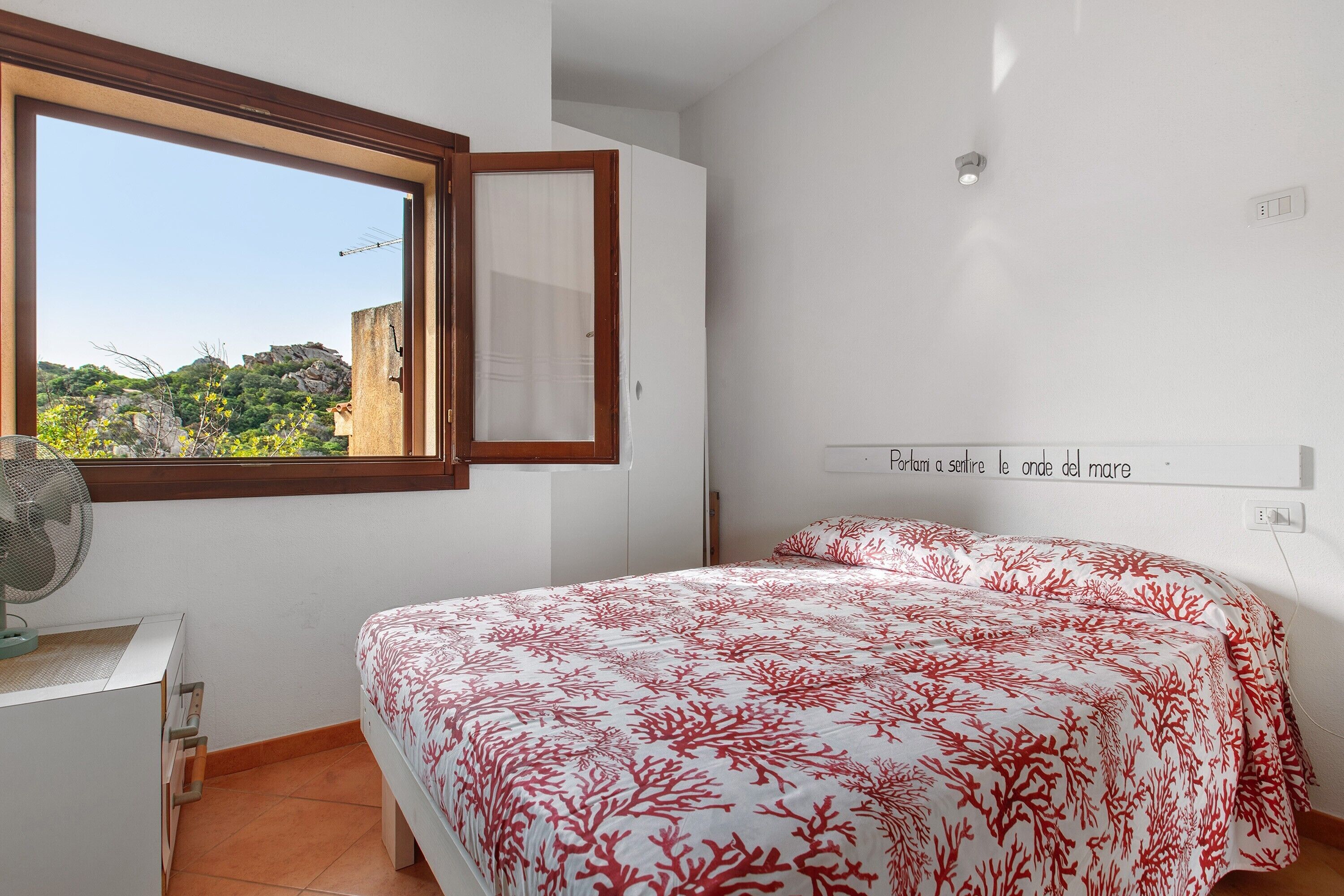 Ein Schlafzimmer mit einem Bett, einem Fenster, einem Ventilator und einer Wandleuchte.