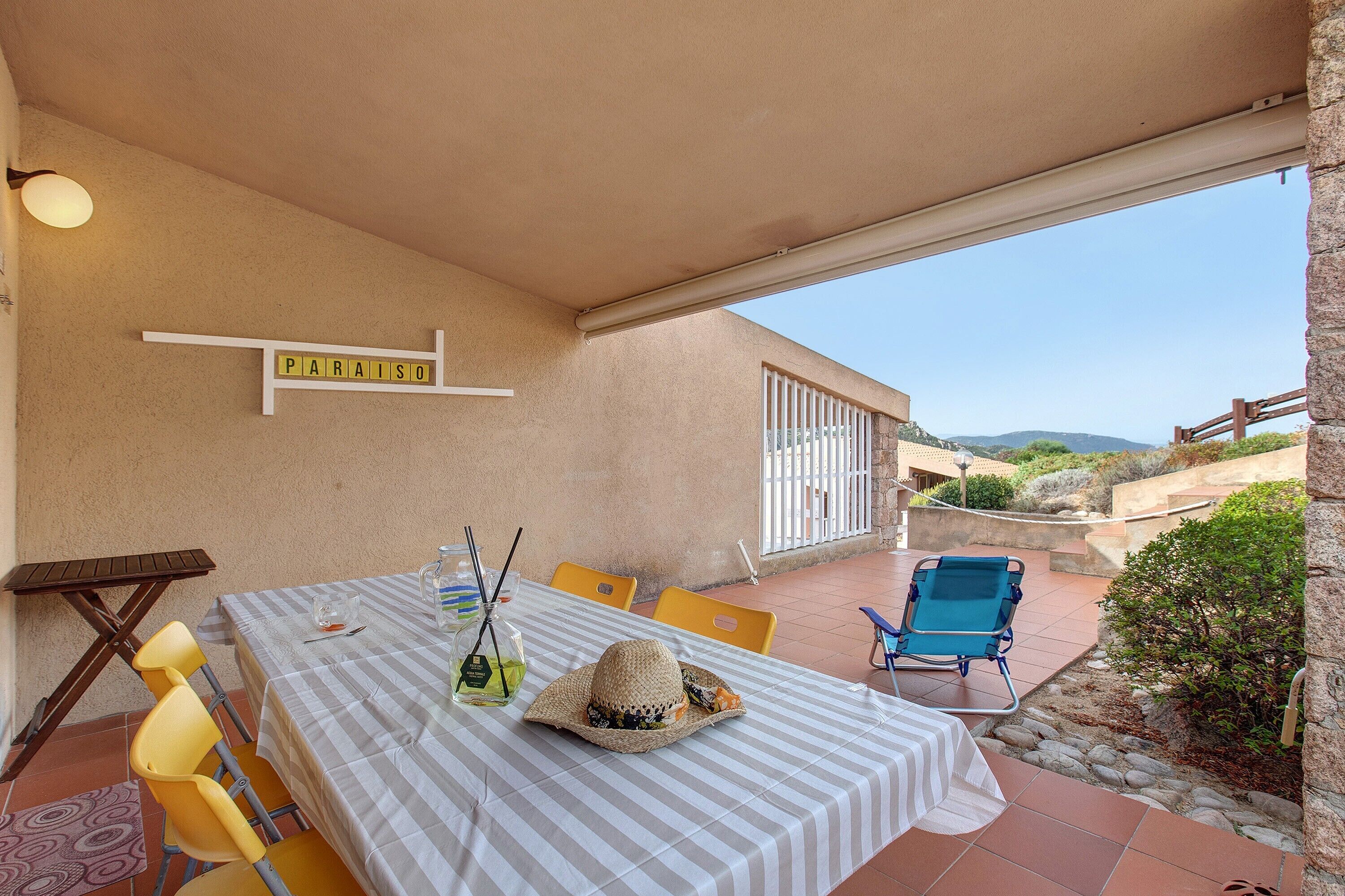 Eine Terrasse im Freien mit einem Tisch für zwei Personen, einem Stuhl, einem Hut und einer Wasserflasche.