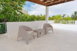 An outdoor patio with two wicker chairs and a small table, surrounded by lush greenery and a white wall. - Luxurious 3 Bedroom Villa With Private Pool in Sosua Ocean Village (Sosúa)