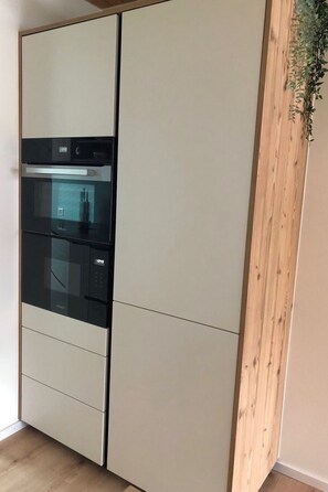 A kitchen with a built-in oven and a wooden accent wall. - Feriensiedlung Trü 23, (Scuol) by Interhome (Scuol)