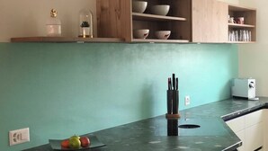Eine Küche mit grüner Wand, Holzschränken, einer schwarzen Arbeitsplatte und einer Obstschale.
