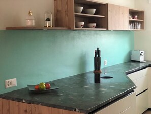 A kitchen with a green wall, wooden cabinets, a black countertop, and a fruit bowl. - Feriensiedlung Trü 23, (Scuol) by Interhome (Scuol)